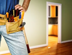 A contractor stands near a doorway with hands on their hips and a belt full of tools